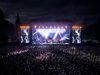 Eine energiegeladene Open-Air-Konzertszene in Osnabrück: Vor einer beeindruckend beleuchteten Bühne feiert ein großes Publikum die Live-Performance der Künstler. Die Bühne ist mit intensiven Lichtshows und einer großen Leinwand ausgestattet, auf der ein Sänger in Aktion zu sehen ist. Diese dynamische Aufnahme vermittelt die lebhafte Atmosphäre und die Begeisterung, die Osnabrücks Veranstaltungskultur prägen.